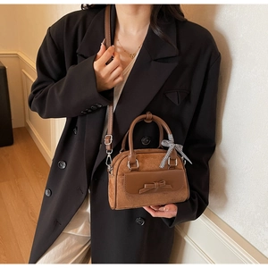 Close-up of brown suede handbag with leather bow detail and checkered scarf decoration