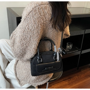 Detail of black shell bag with leather bow and plaid ribbon on a beige sweater