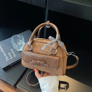 Detailed view of a brown suede handbag with leather bow flap and checkered ribbon handle