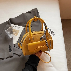 Yellow suede shoulder bag with bow detail and plaid ribbon shown in lifestyle setting