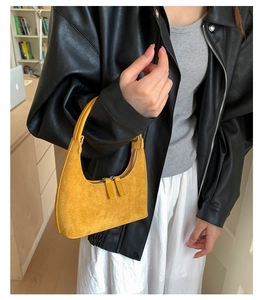 Detail of yellow suede crescent bag with silver dual zippers held by a model in a black coat