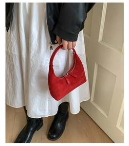 Close-up of a vibrant red crescent shoulder bag with silver zipper and suede texture