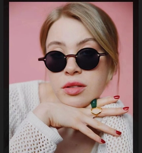 Close-up of black round frame sunglasses and vintage rings on a pink background