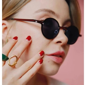 Close-up of black round sunglasses with red and black striped temples on a female model