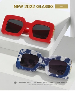 Close-up of red and marble pattern square sunglasses with gold metal hinge detail