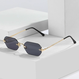 Rimless octagonal sunglasses with grey lenses and gold metal frame on a white block