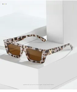 Detail of leopard print rectangle sunglasses featuring a gold X-shaped metal logo on the temple