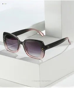 Detail of square gradient sunglasses with gold rivet accents on geometric stand