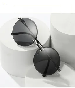 Close-up of rimless round sunglasses with grey lenses and slim metal temples on white pedestal
