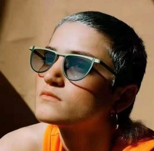 Close-up of geometric green sunglasses with blue gradient lenses on a fashion model