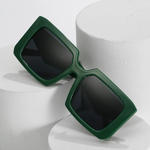 Fashionable dark green square frame sunglasses with black lenses on white stone pedestal