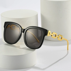 Chic black square sunglasses featuring a statement gold chain temple on white pedestals