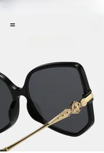 Close-up of black frame sunglasses with golden floral metal logo on the temple