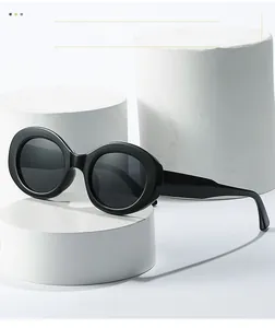 Detail of black oval sunglasses featuring thick frames on a white cylindrical stand