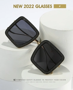 Close-up of black glitter square sunglasses with gold metal bridge on white display