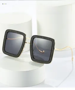 Detail showing square frame sunglasses with black glitter texture and gold wavy metal legs