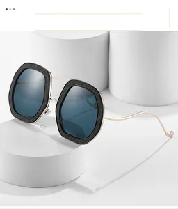Détail de lunettes de soleil carrées pailletées noires avec branches dorées ondulées