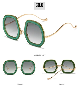 Detail view of green glitter hexagonal sunglasses with wavy gold metal arms and gradient lenses
