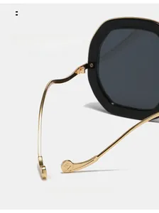 Detail of curved gold metal legs and geometric logo on black oval sunglasses