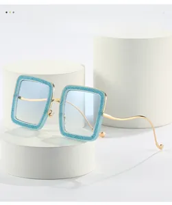 Detail of square sunglasses with blue glitter edges and golden wavy metal temples