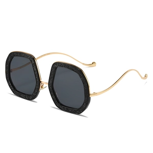 Oversized black glitter octagon sunglasses with golden wavy temples on white background