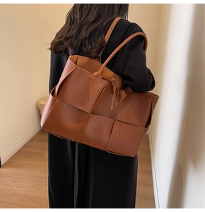 Detail of caramel woven tote bag featuring wide leather straps and tie closure detail