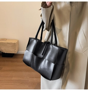 Detail of a large black woven leather tote bag with wide weave texture and long handles