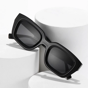 Fashionable black square sunglasses with dark lenses displayed on minimalist white pedestals