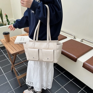 Detail of a creamy white tote bag with dual front pockets and silver snap fasteners