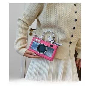 Pink camera-shaped crossbody bag with rhinestone accents and silk scarf handle detail