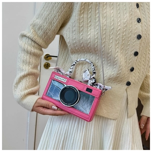 Close-up of pink camera-shaped crossbody bag with decorative feathers and printed silk scarf