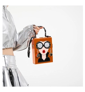 Détail du sac boîte orange avec motif portrait mode et foulard à pois sur l'anse