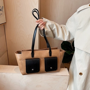 Detail of camel and black color-block handbag with dual front pockets on wood background