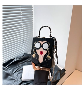 Détail du sac boîte noir verni avec motif mode, chaîne dorée et poignée ornée d'un foulard