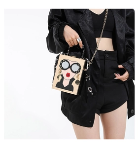 Détail d'un sac boîte doré orné d'un visage pop-art avec lèvres rouges et lunettes