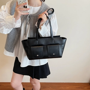Detail of black tote bag featuring dual front pockets with silver metal buckle accents