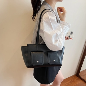 Detail of black faux leather tote bag featuring two front pockets with silver metal studs