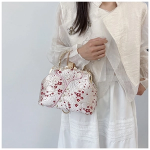 Detailed close-up of vintage embroidered handbag with pearl clasp and plum blossoms