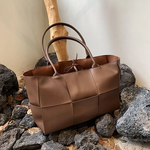 Large dark brown woven leather tote bag shown in a natural aesthetic scene