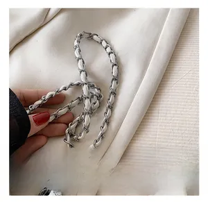 Dettaglio della catena in metallo argento intrecciata con pelle bianca e fermagli metallici