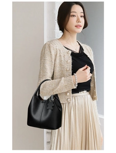 Detail of black lychee grain leather bucket bag featuring a cute bear charm and chain