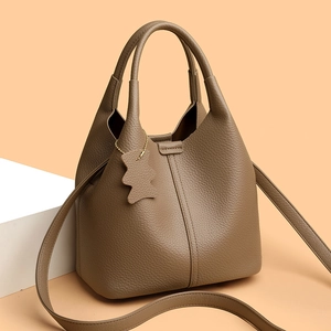 Close-up of litchi texture on dark beige bucket bag with bear pendant and strap