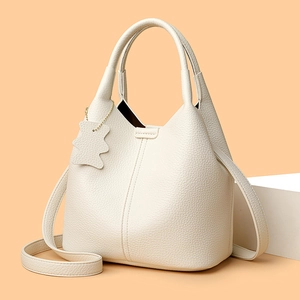 Detailed shot of cream bucket bag showing premium lychee grain leather and bear charm