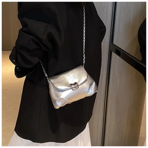 Dettaglio della borsa a tracolla argento metallizzato con catena su un blazer nero