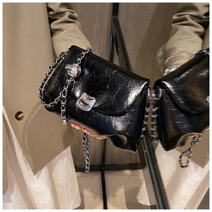 Dettaglio borsa in pelle nera a pieghe con catena d'argento e ciondolo floreale in metallo