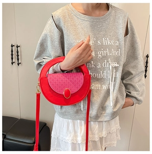 Detail of red circular crossbody bag with woven pink flap and top handle on model