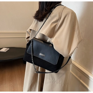 Side view of black leather chain bag with silver logo on beige trench coat outfit