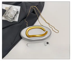 Silver oval evening clutch bag with gold ring handle and chain strap for size reference