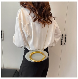 Light gray oval crossbody bag with large gold C-buckle shown on a shoulder strap