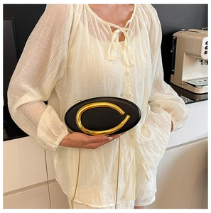 Detail of elegant black leather oval bag with striking gold C-buckle and fine chain strap